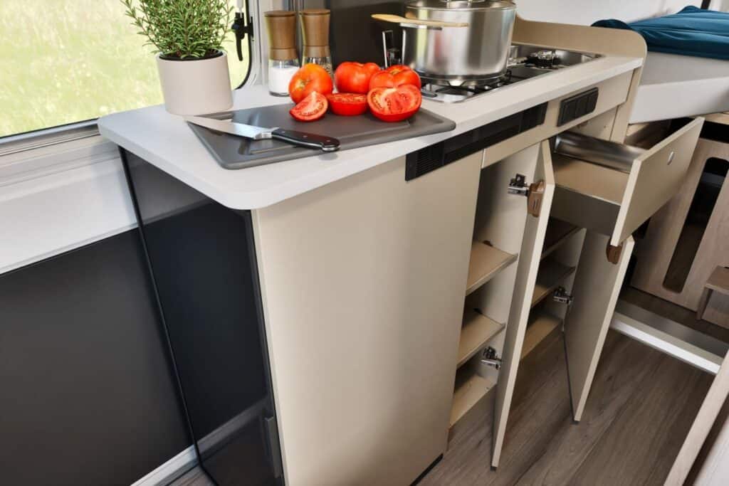 Moderne buscamper keuken met compact opbergkast, gaskookplaat en verse ingrediënten.