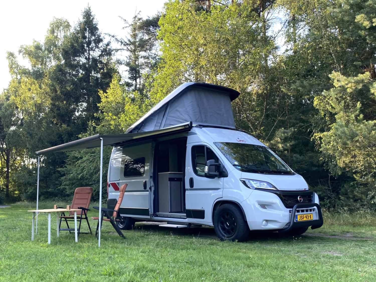 Hefdak van de buscamper open op de camping, met zicht op de ingerichte slaapplek