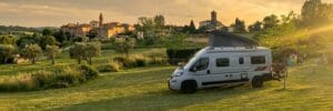 Buscamper met hefdak (LMC Innovan 600) op camping in Toscane bij zonsondergang, hefdak volledig open